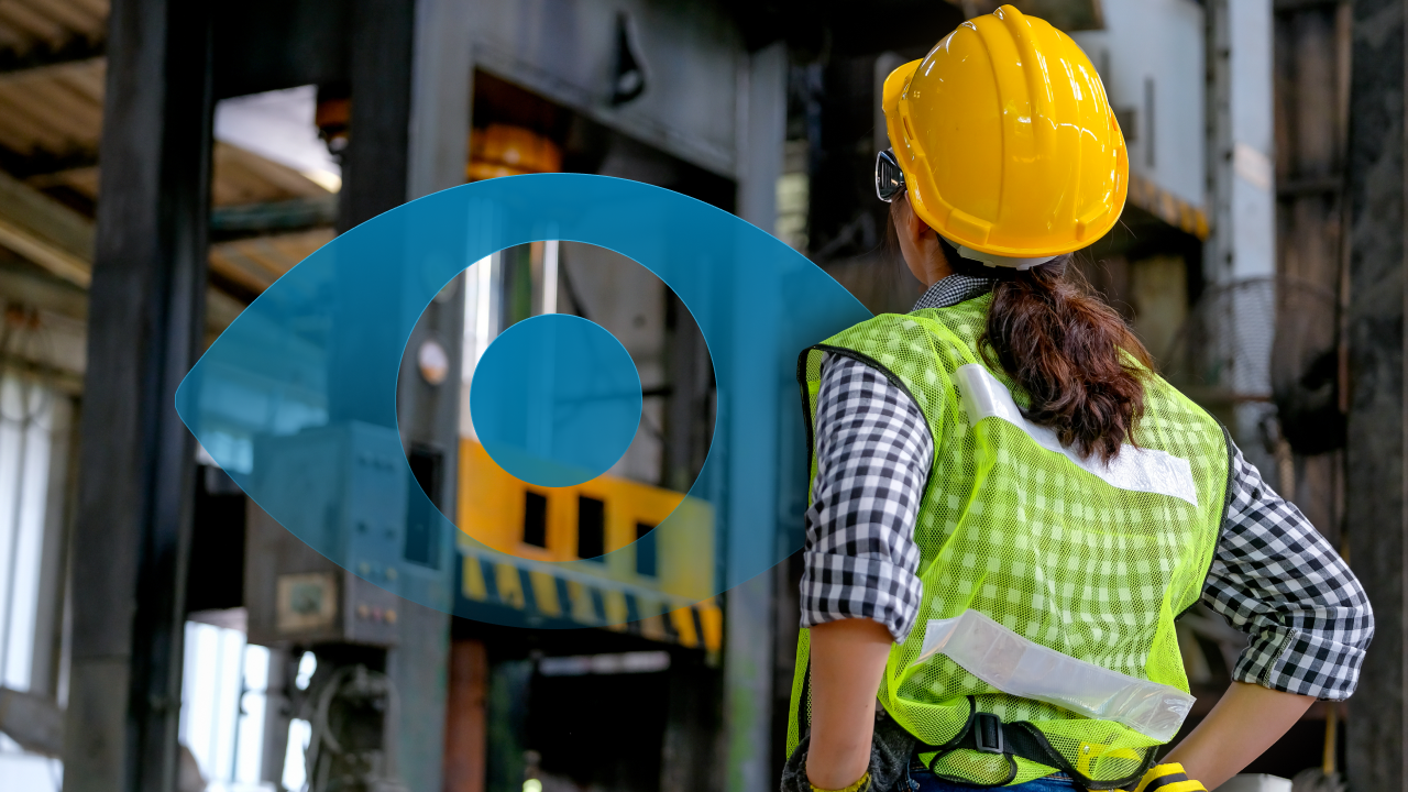 In the feature image for a blog post about Visual Factory, a woman wearing a hard hat and safety vest poses next to a large machine.