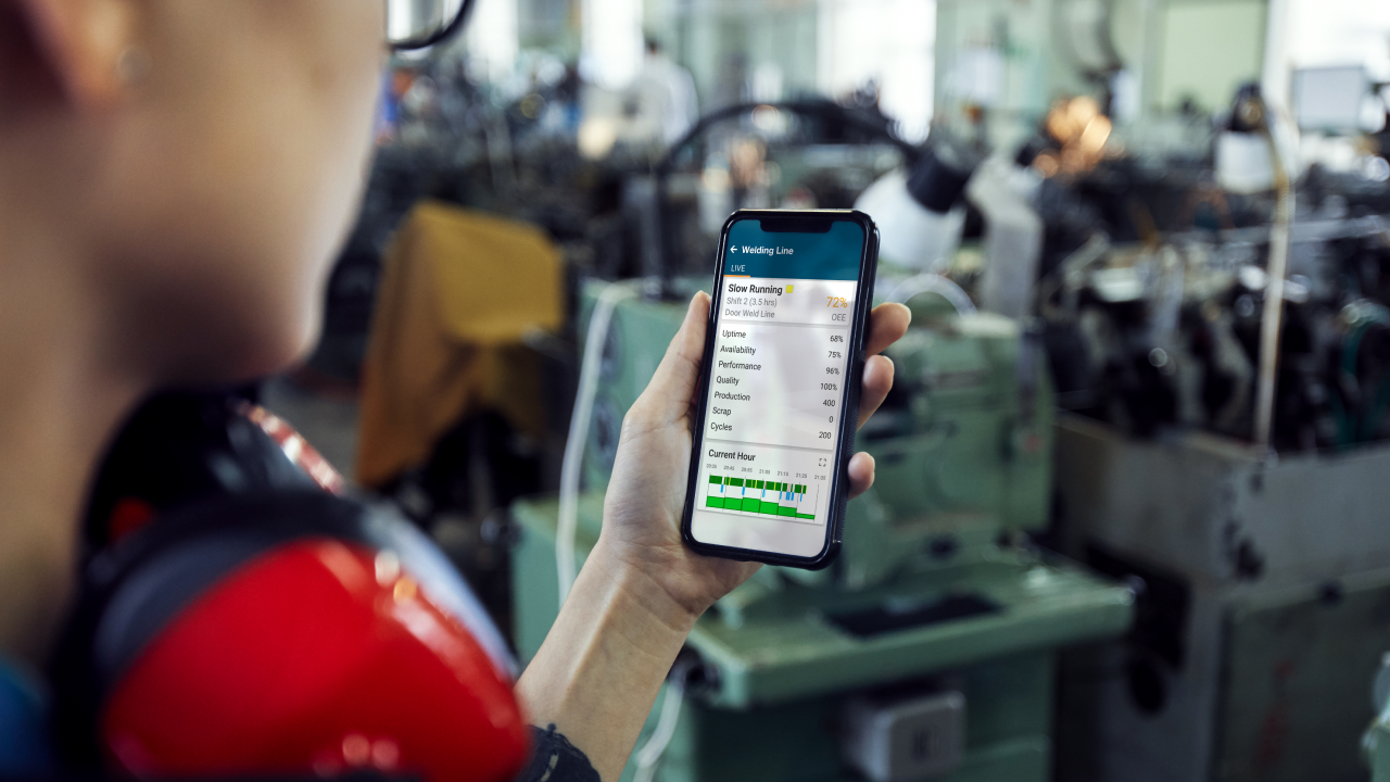 Shop floor worker monitoring manufacturing process on his smartphone.