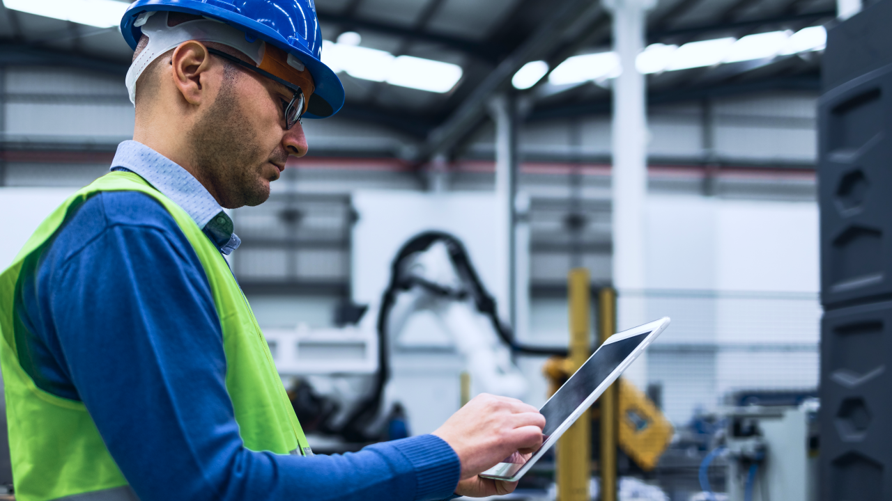 Portrait of Professional Heavy Industry Engineer / Worker Wearing Safety Uniform and Hard Hat Uses Tablet Computer. In the Background Construction Factory.